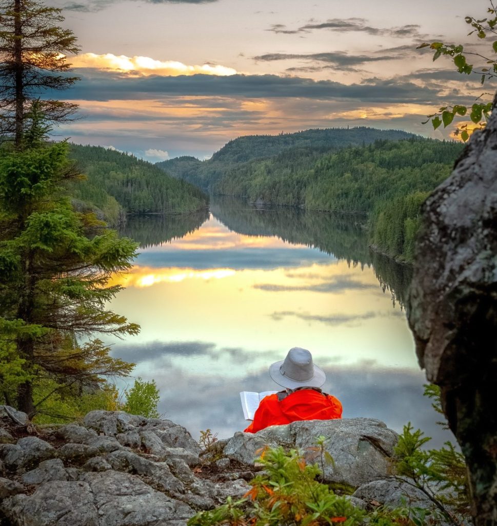 Une personne en pleine lecture confortablement installée sur des roches avec vue sur le lac au par national d'Aiguebelle.